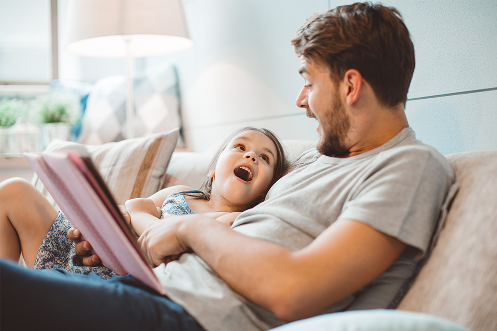 adult male and female child sitting on a couch reading a book