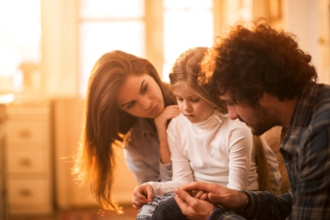 An older man and two young children sitting on a couch smiling in a warm embrace.