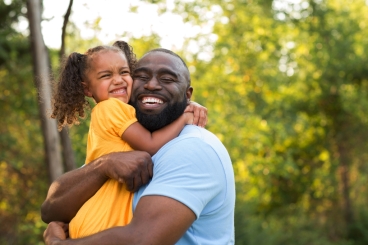 Black man hugging a young girl smiling.