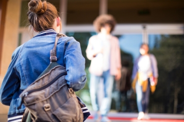 Woman wearing a backpack walking towards a building.