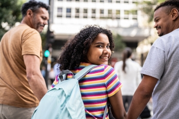Two men and girl walking together while holding hands and smiling.