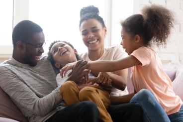 Adult male and female sitting on sofa with a young boy and girl, laughing.