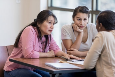 Woman and teenage girl sit across from another woman with serious expressions.