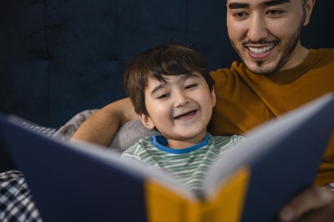 Man and young boy smiling as they look at a book they are holding.
